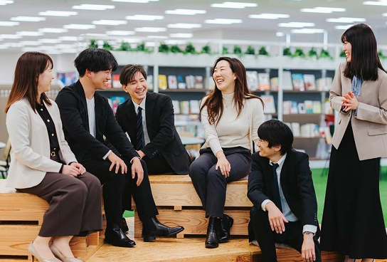 積み重ねられたウッドデッキに座った6人の男女が笑顔で語り合っている写真