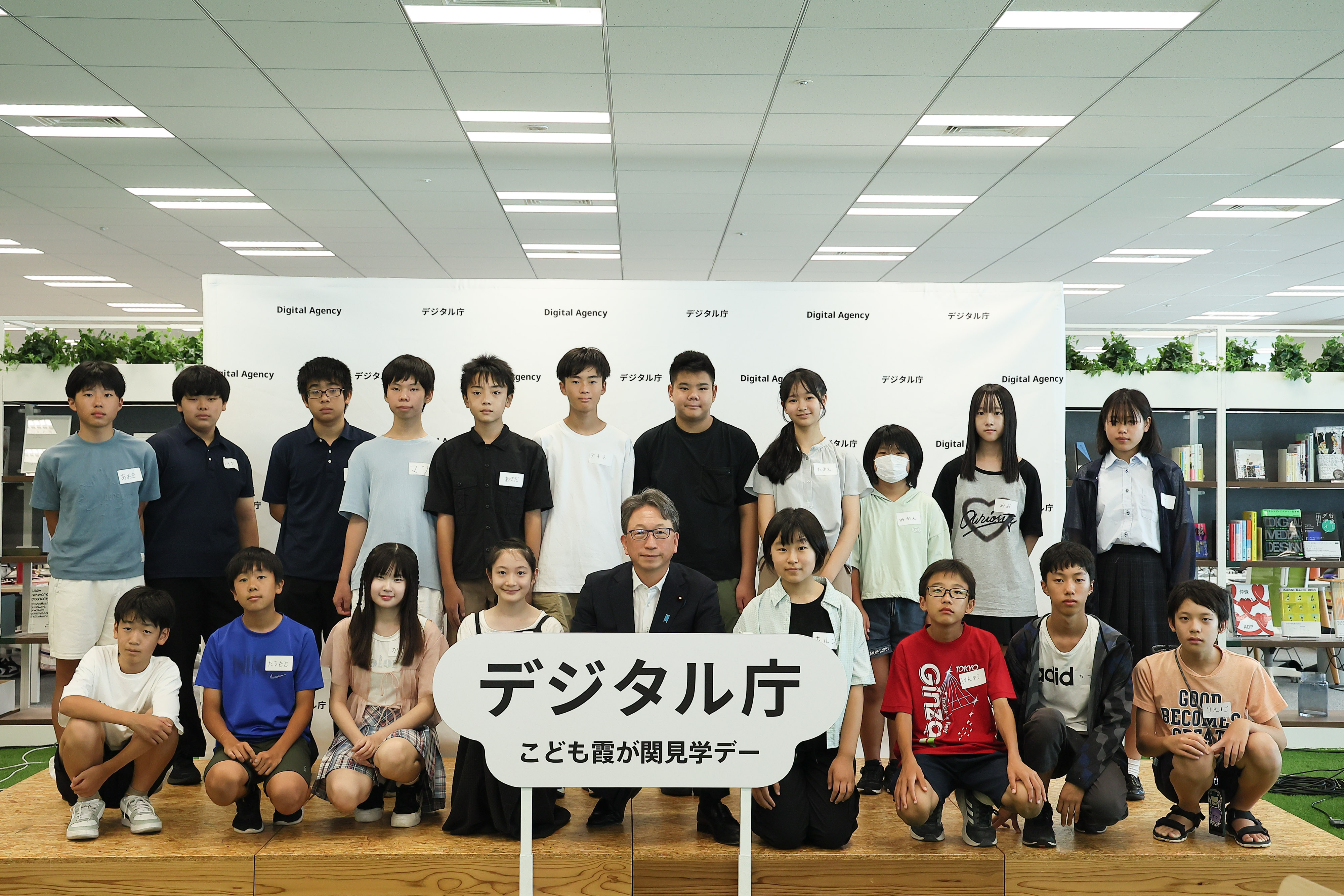 「デジタル庁 子ども霞が関見学デー」のロゴパネルが真ん中に飾られているステージの上で、ワークショップに参加した中学生と平デジタル大臣が2列に並んでいる。前列はしゃがんでおり、後列は立っている。