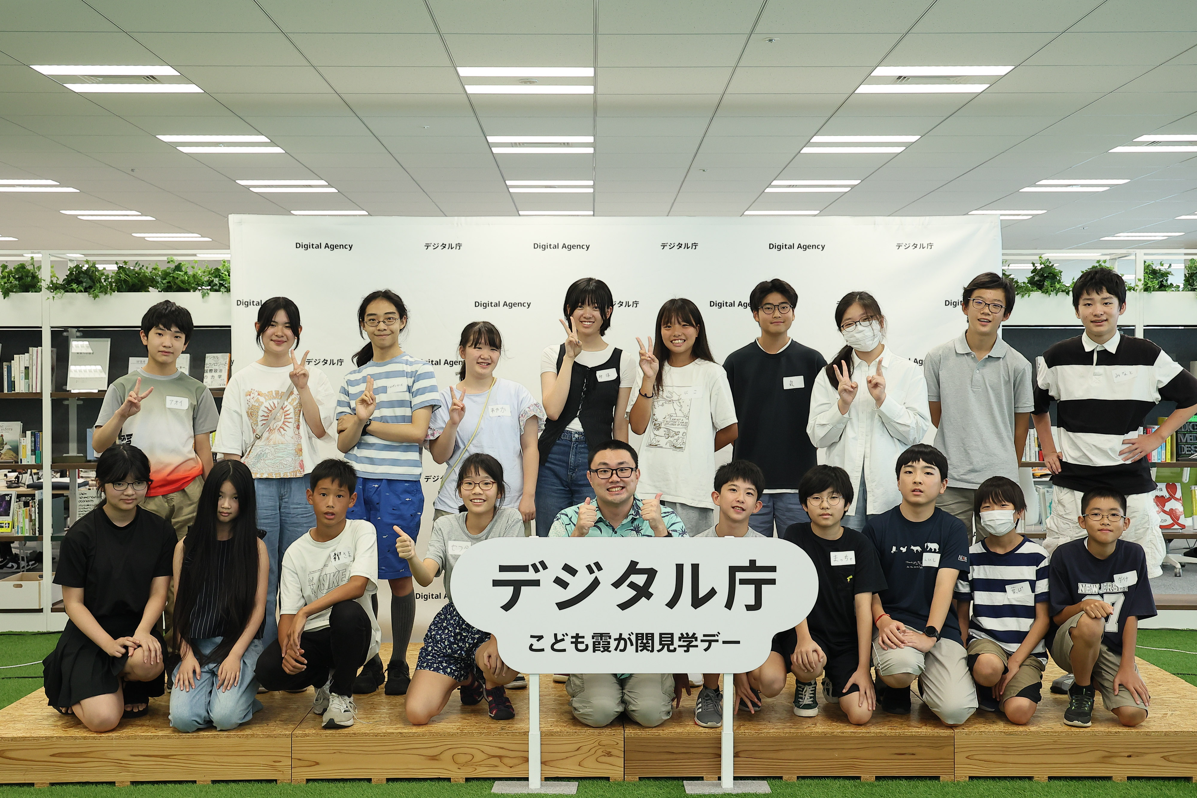 「デジタル庁 子ども霞が関見学デー」のロゴパネルが真ん中に飾られているステージの上で、ワークショップに参加した中学生とデジタル庁AI担当 データサイエンティスト大杉が2列に並んでいる。前列はしゃがんでおり、後列は立っている。
