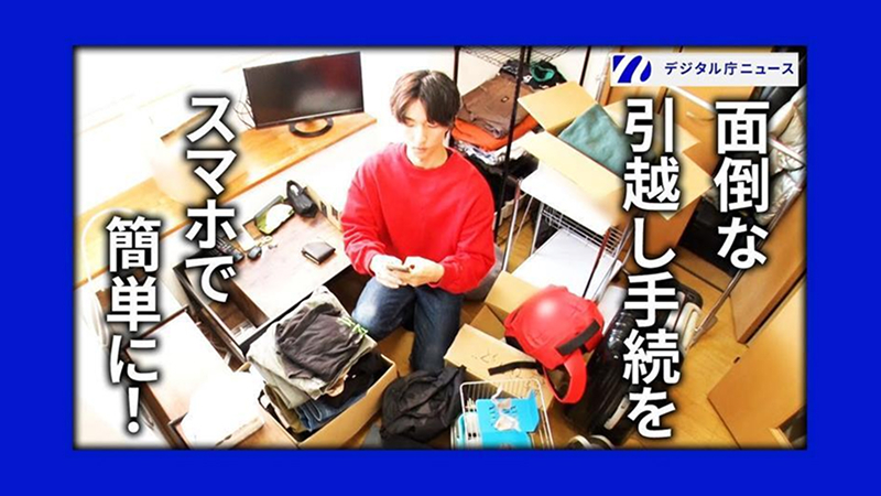 デジタル庁ニュースの動画サムネイル画像。右上に「デジタル庁ニュース」のロゴ。右側に白い太字で「面倒な引越し手続きを」、左側に「スマホで簡単に!」と大きく記載されている。写真には、段ボール箱や荷物が散乱した引越し中の部屋の中央に、赤いスウェット姿の男性が座り、スマートフォンを操作している様子が俯瞰で撮影されている。