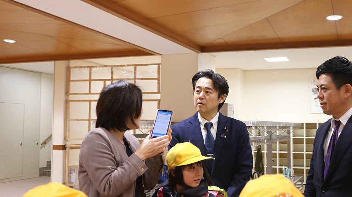 Mr. Hosaka, State Minister for Digital Transformation, is standing with Samisa in the elementary school building and exchanging opinions with the parents.