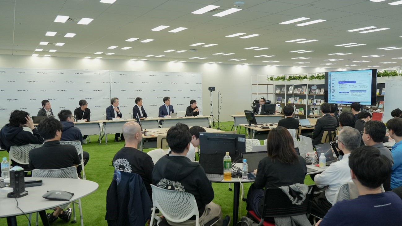 Six commentators, including Minister for Digital Transformation TAIRA Masaaki of Digital Agency, are reviewing the prototype of the AI developed at the event. Commentators are seated side by side in the front of the venue, and participants are listening to the reviews. 