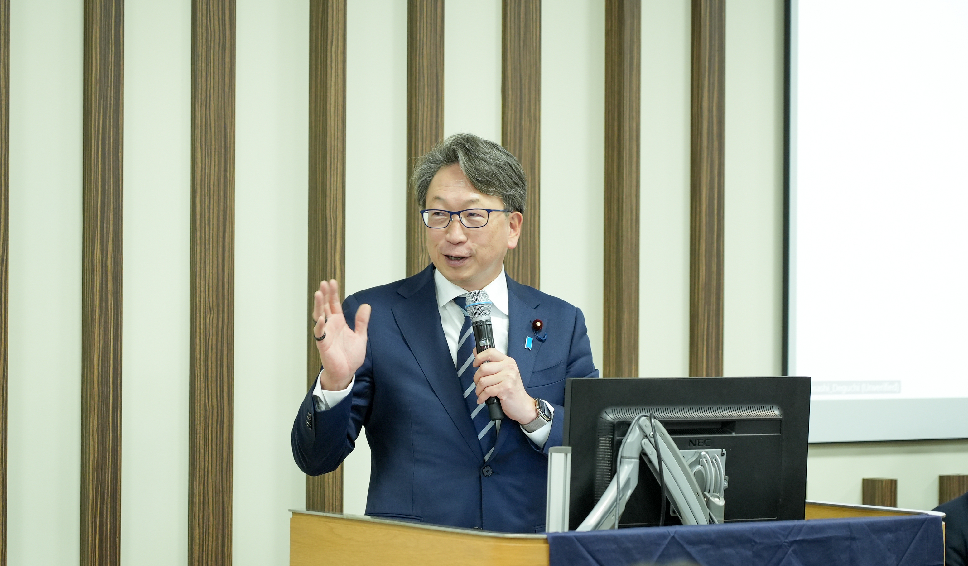 Minister Hirata delivers a speech from the platform at the hackathon. 