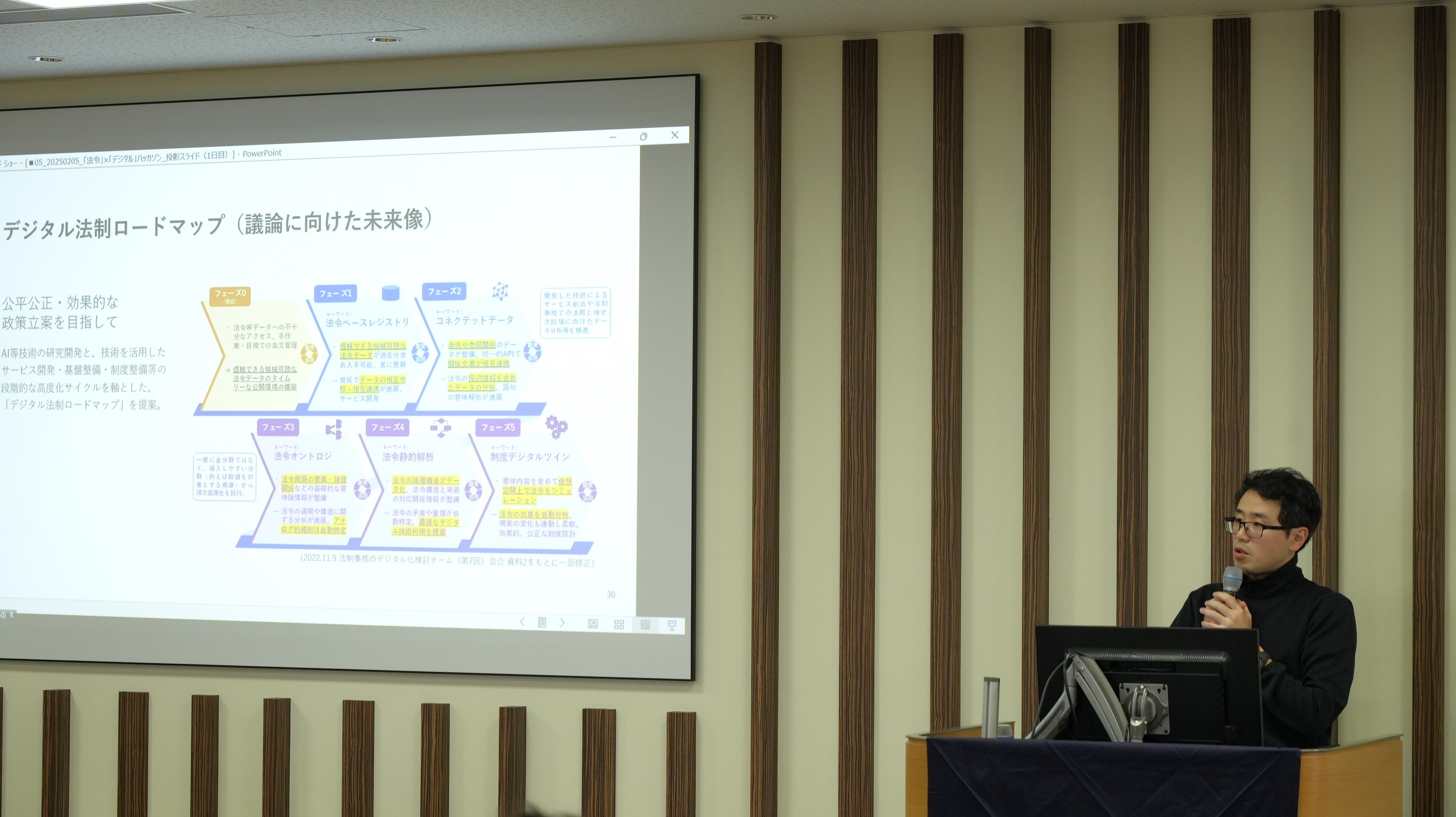 A picture of the Digital Agency's Nakano Director for Policy Planning introducing its efforts. On the screen next to the Nakano Director for Policy Planning, the Digital Legislation Forum is projected. 